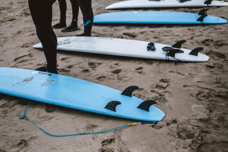 Surfboards lined up on a sandy beach, surfers prepare for ocean adventures.